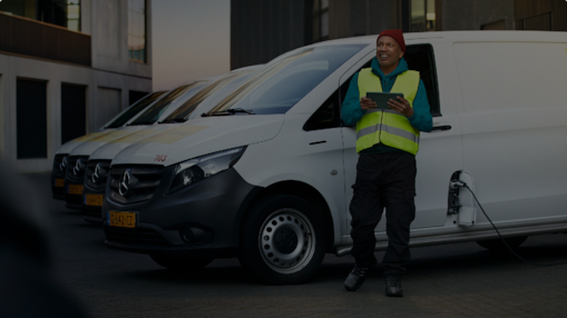 Ein Mann steht mit einem Tablet in der Hand vor mehreren E-Transportern, die aufgeladen werden