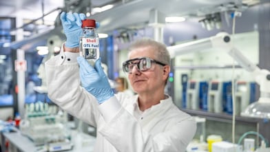 Labormitarbeiter der ein Fläschen GTL Fuel hochhält