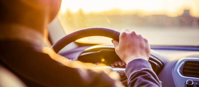 Ein Mann fährt im Auto. Blick von hinten nach vorne mit Hand am Lenkrad.