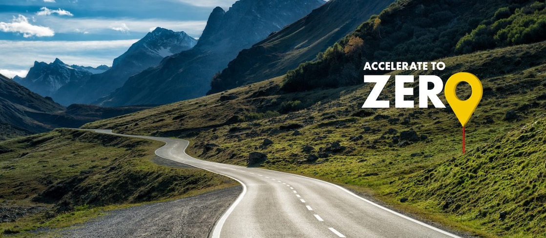 Auto fährt auf einer Schnellstraße durch grüne Landschaft mit Bergen im Hintergrund, Textaufschrift: "Accelerate to Zero".