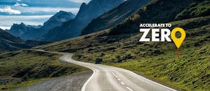 Auto fährt auf einer Schnellstraße durch grüne Landschaft mit Bergen im Hintergrund, Textaufschrift: "Accelerate to Zero".