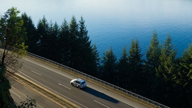 Ein Auto fährt auf einer Straße an einem See.