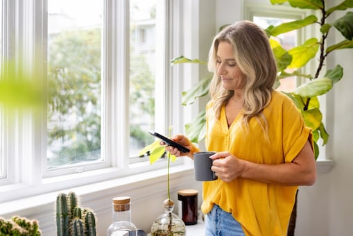 Eine Frau sieht auf ihr Smartphone und trinkt einen Kaffee.