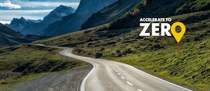 Auto fährt auf einer Schnellstraße durch grüne Landschaft mit Bergen im Hintergrund, Textaufschrift: "Accelerate to Zero".