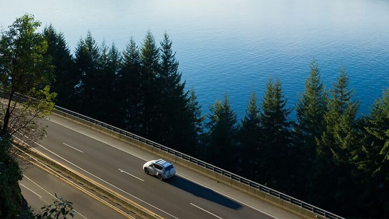 Ein Auto fährt auf einer Straße an einem See.