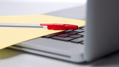 Laptop mit einem roten Kugelschreiben auf einem gelben Blatt Papier