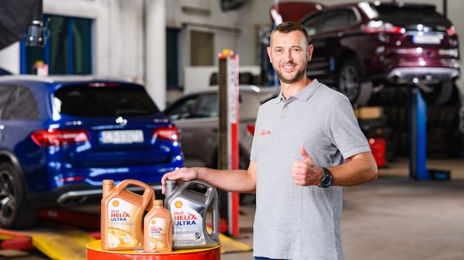 Kfz‑Mechaniker in moderner Autowerkstatt präsentiert Shell Helix Ultra Motoröle (0W‑30, 5W‑30) vor angehobenen Fahrzeugen – hochwertige Motoröle für optimalen Motorschutz und Leistung