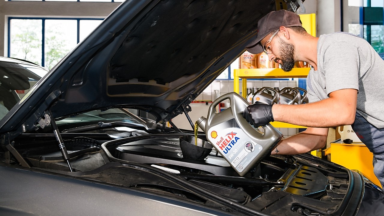 Motorölwechsel in der Werkstatt: Fachkraft füllt Shell Helix Ultra Motoröl in den Motor eines Pkw – optimale Schmierung, Motorschutz und Leistungsfähigkeit durch hochwertige Shell Schmierstoffe.