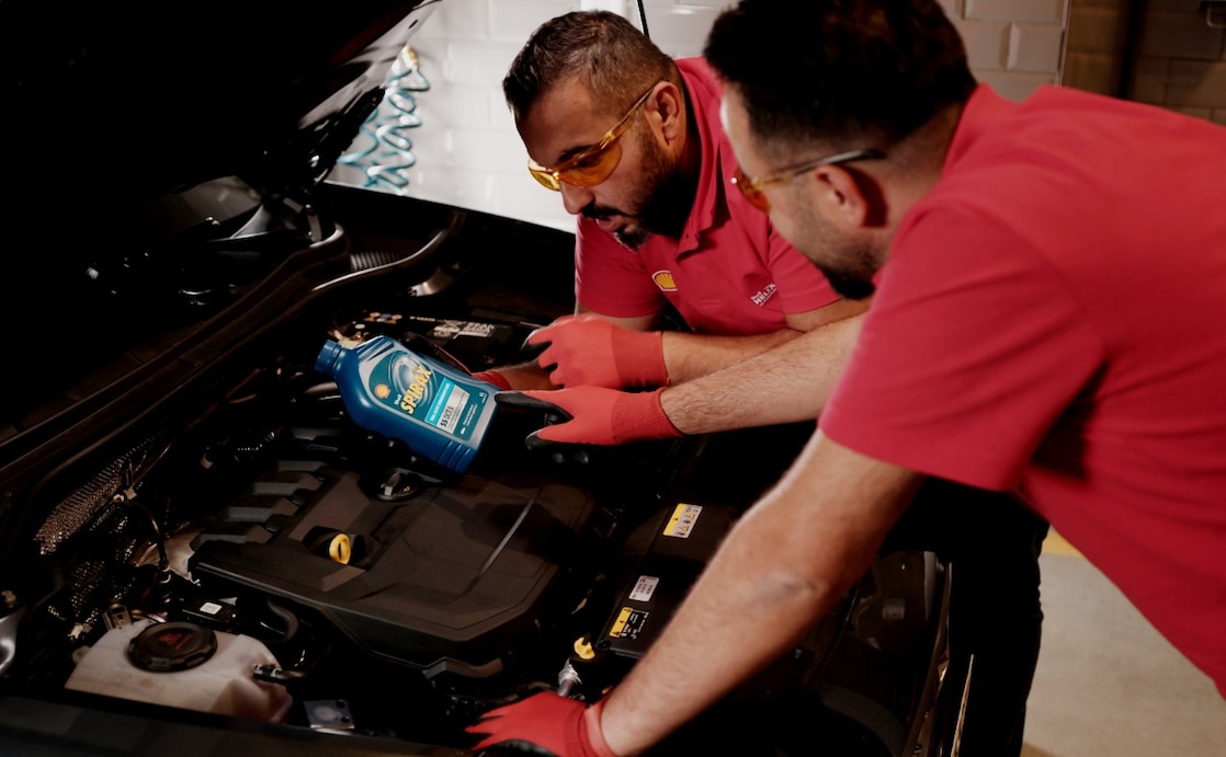 Mechaniker in Shell-Arbeitskleidung füllen Shell Spirax Getriebeöl in den Motorraum eines Fahrzeugs ein.