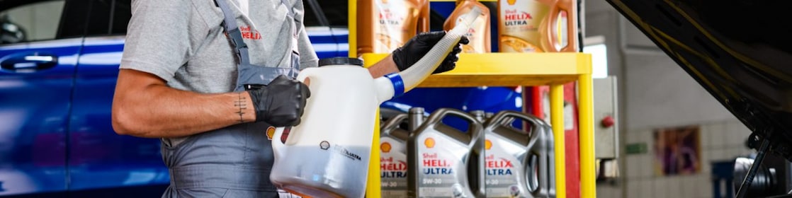 Mechaniker beim Befüllen eines Fahrzeugs mit Motoröl in einer Werkstatt, im Hintergrund stehen verschiedene Motorölkanister von Shell Helix