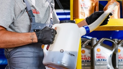 Mechaniker beim Befüllen eines Fahrzeugs mit Motoröl in einer Werkstatt, im Hintergrund stehen verschiedene Motorölkanister von Shell Helix