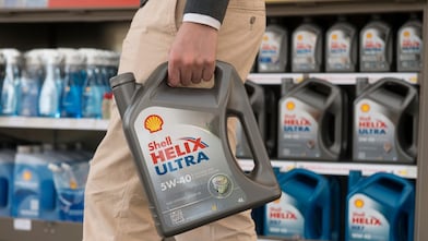Person hält einen 4‑Liter‑Kanister Shell Helix Ultra 5W‑40 Motorenöl vor einem Regal mit weiteren Shell‑Motorenölen in einem Geschäft; Produktetikett und Markenlogo sind klar sichtbar.