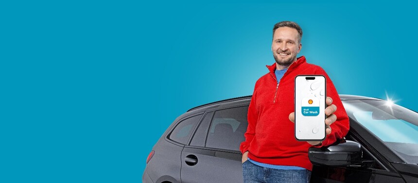 Hand mit Smartphone vor weißem Hintergrund mit Wassertropfen. Im Screen ist das App-Icon der neuen Shell Car Wash App mit Shell Muschel zu sehen.
