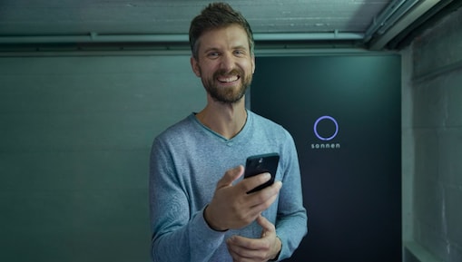 Lächelnder Mann mir einem Smartphone vor einer sonnen Batterie