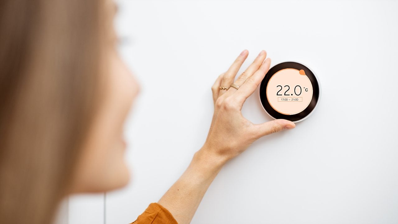 Frau bedient Temperaturregler an Wand in ihrem Zuhause