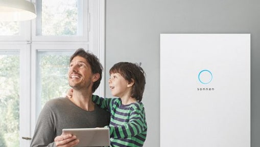 Ein Mann mit einem Tablet und einem Kind im Arm vor einer sonnenBatterie