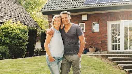 Eine Frau lädt ihr Elektroauto vor ihrem Haus mit Sonnenkollektoren auf