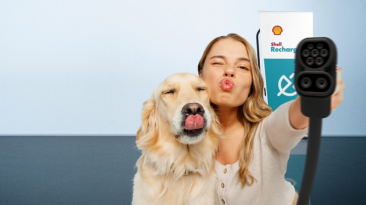 Frau hält einen Hund und einen EV-Ladestecker; daneben steht ein blaues Elektroauto.