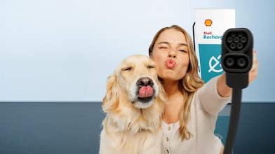 Frau hält einen Hund und einen EV-Ladestecker; daneben steht ein blaues Elektroauto.