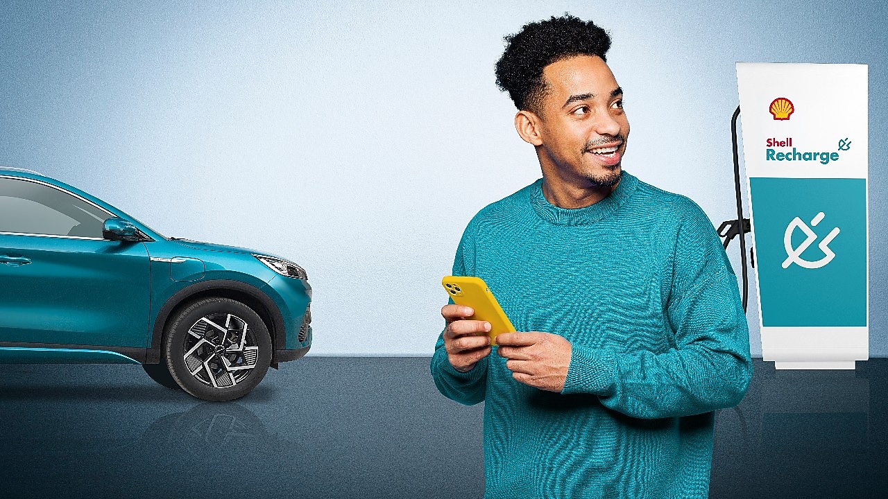 Ein Mann mit gelbem Smartphone steht neben einem blauen BYD E-Auto und einer Shell Recharge Ladestation.