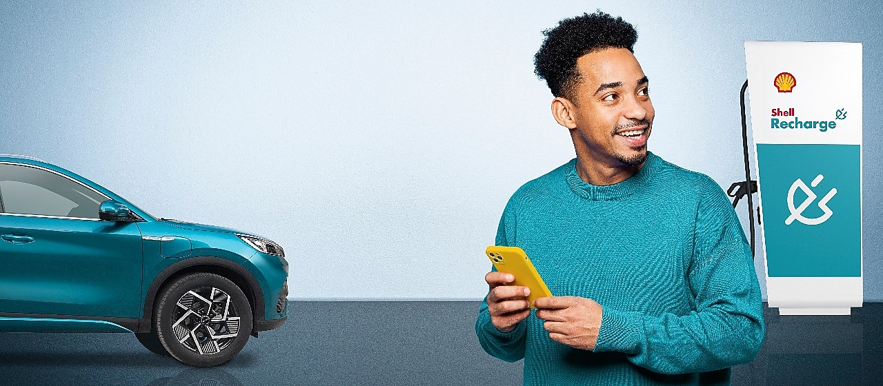 Ein Mann mit gelbem Smartphone steht neben einem blauen BYD E-Auto und einer Shell Recharge Ladestation.