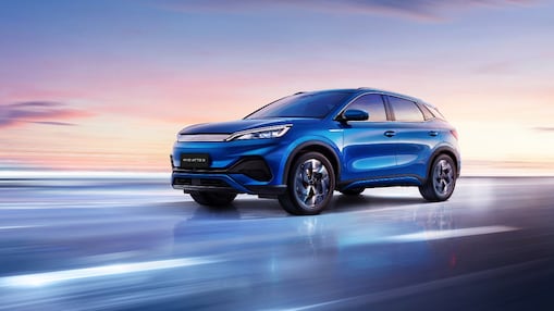 Ein blaues BYD-Auto, das auf einer blauen Straße mit einem rosa Sonnenuntergangshimmel fährt