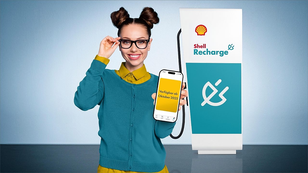 Junge Frau hält lächelnd den Ladestecker einer Shell Recharge Ultraschnellladesäule in der Hand.
