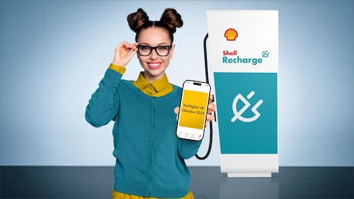 Junge Frau hält lächelnd den Ladestecker einer Shell Recharge Ultraschnellladesäule in der Hand.