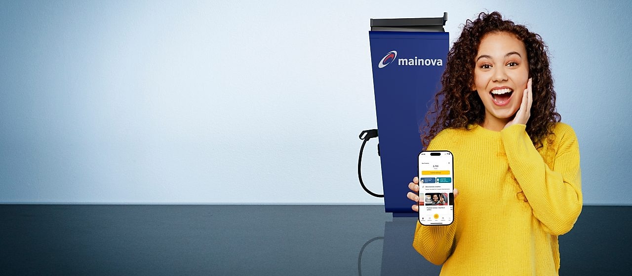 Eine Frau mit gelbem Pulli und Smartphone, auf dem die Shell App zu sehen ist, steht neben einer Mainova Ladestation.