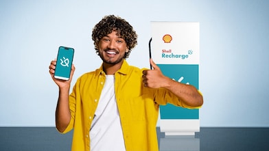 Mann mit gelbem Hemd und Handy in der Hand vor Shell Recharge Ladesäule