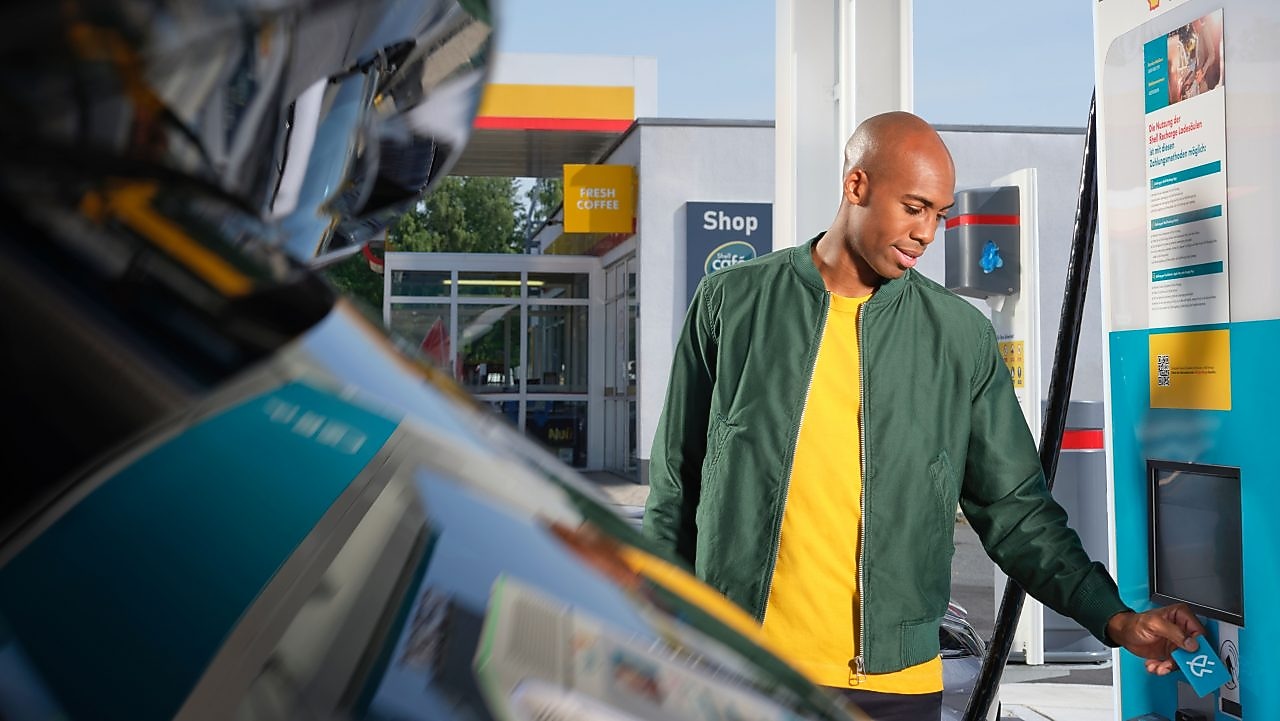 Hand hält einen Shell Café Kaffee Becher vor türkisem Grund. Text auf gelbem Störer: GRATIS Heißgetränk.