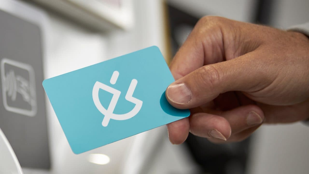 Hand hält einen Shell Café Kaffee Becher vor türkisem Grund. Text auf gelbem Störer: GRATIS Heißgetränk.