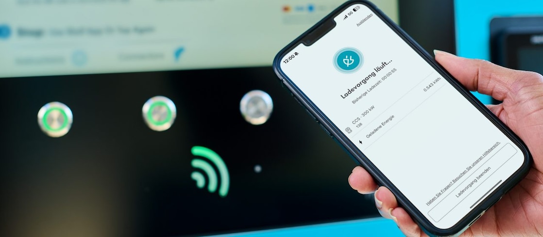Smartphone vor einer E-Ladestation während eines aktiven Ladevorgangs mit der Shell App.