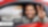 Ein Mann sitzt in einem roten Auto. Er ist angeschnallt und lächelt. Das Seitenfenster ist komplett unten, sodass er seinen Arm lässig hinaushält und mit seiner Hand das Victory-Zeichen macht. Im Hintergrund erkennen wir in der Unschärfe eine Shell Tankstelle.