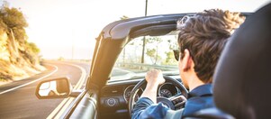 Junger Mann mit Sonnenbrille fährt im Cabrio der Sonne entgegen