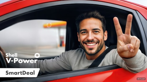 Ein Mann sitzt in einem roten Auto. Er ist angeschnallt und lächelt. Das Seitenfenster ist komplett unten, sodass er seinen Arm lässig hinaushält und mit seiner Hand das Victory-Zeichen macht. Im Hintergrund erkennen wir in der Unschärfe eine Shell Tankstelle.