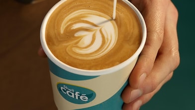 Barista schenkt Milchkaffee in einen Shell Café Becher ein