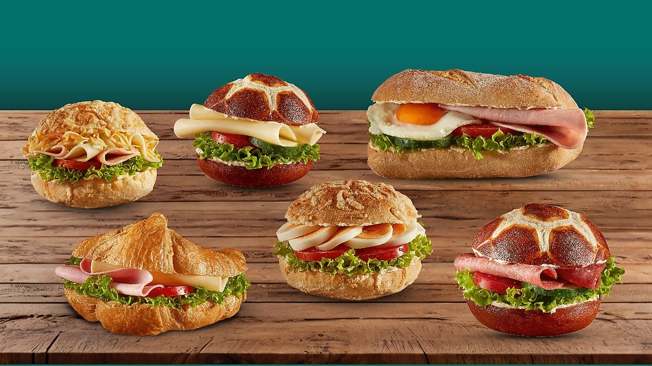 Verschiedene belegte Brötchen und ein Croissant mit frischen Zutaten auf Holztisch. Auswahl an herzhaften Snacks im Shell Café Backshop.