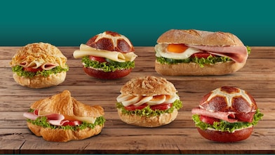 Verschiedene belegte Brötchen und ein Croissant mit frischen Zutaten auf Holztisch. Auswahl an herzhaften Snacks im Shell Café Backshop.