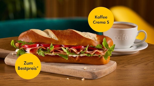 Rustico-Sandwich mit Schinken, Tomate und Rucola auf einem Holzbrett neben einer Tasse Shell Café Kaffee Crema S. Zwei gelbe Störer überlagern das Bild mit den Texten „Kaffee Crema S“ und „Zum Bestpreis*“.
